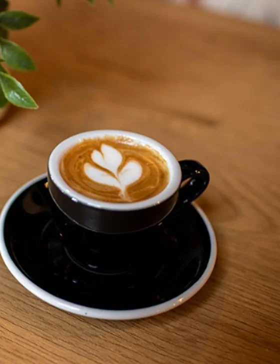 Café con arte latte en taza negra sobre plato